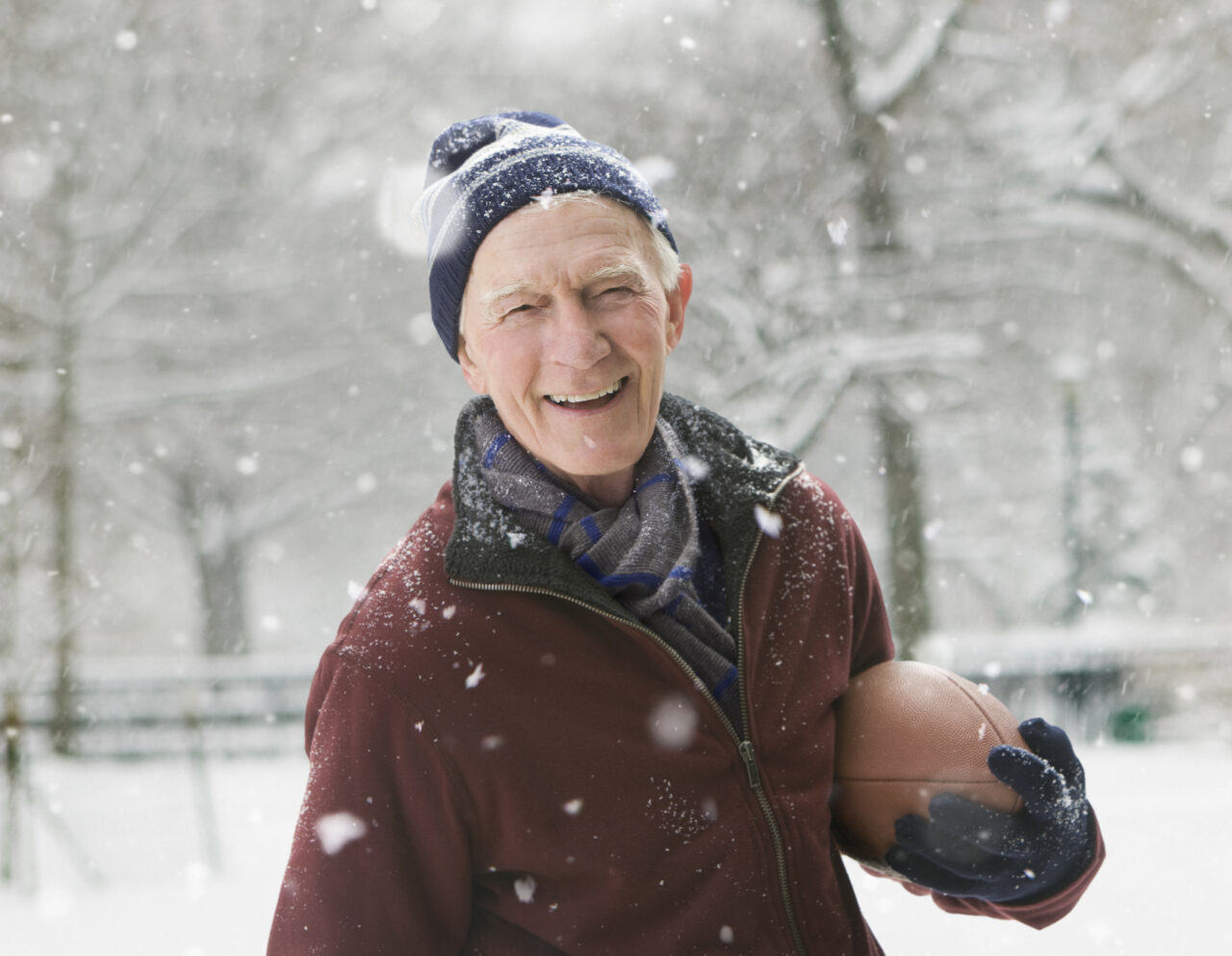 Elderly man holding a football smiling during snow storm